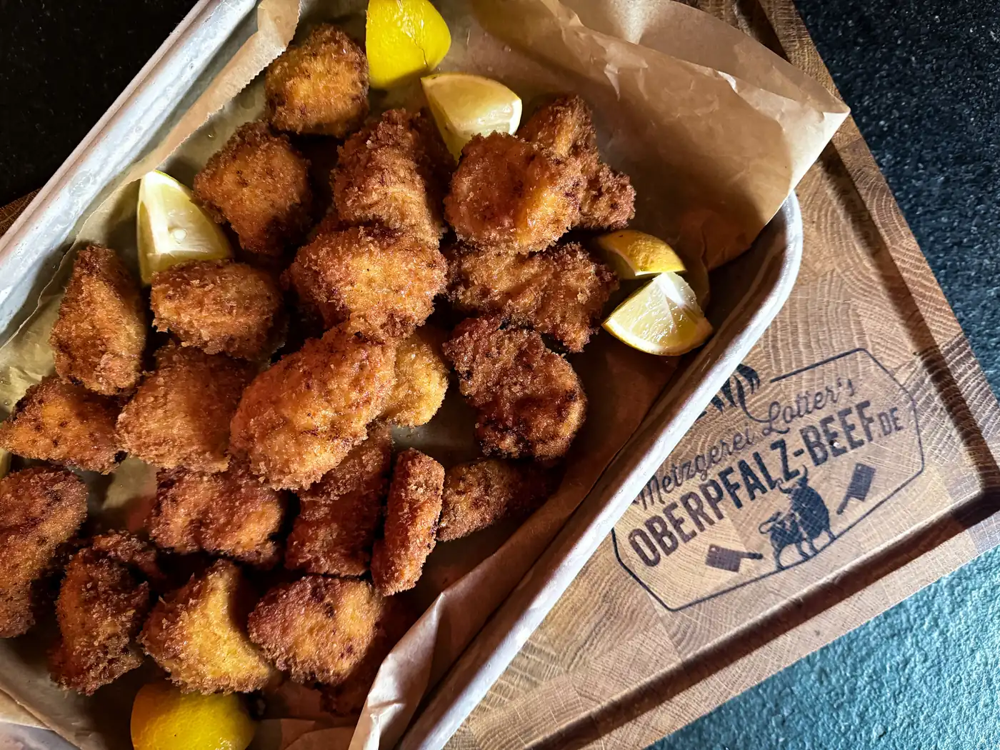 Knusprig frittierte Hähnchenstücke mit Zitronenspalten auf dem Brett