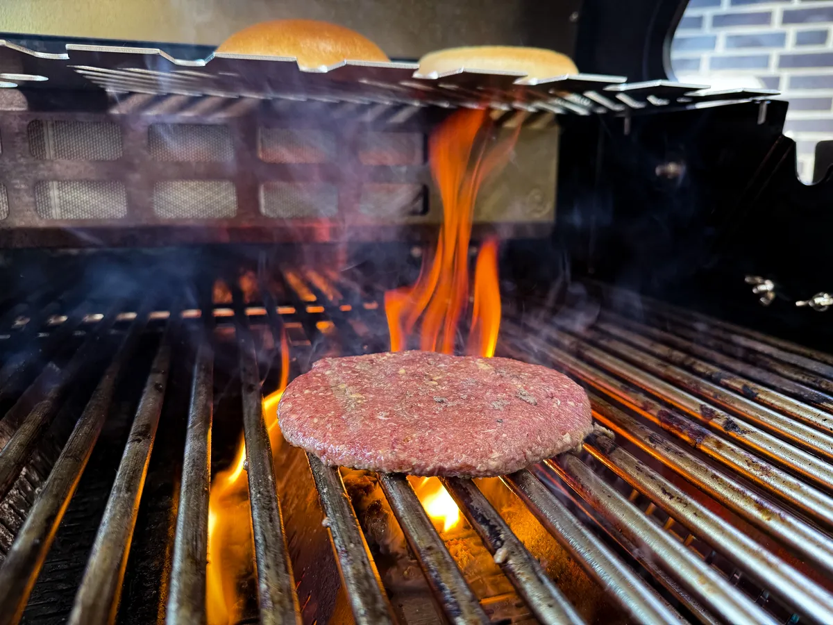 Burger-Patty auf dem Grillrost über offener Flamme