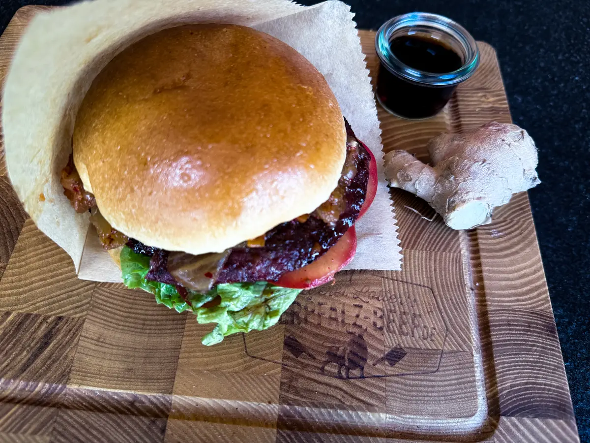 Kimchi-Burger mit Salat und Tomate im Brioche-Bun, daneben Ingwer und Sojasauce