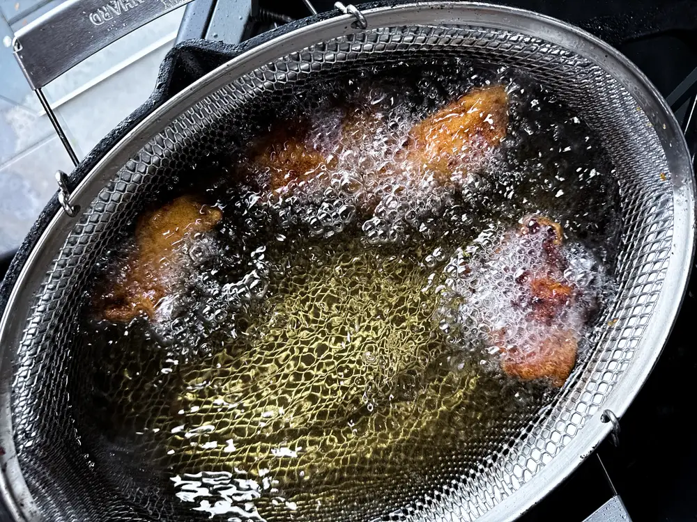 Hähnchenkeulen werden im Frittierkorb goldbraun frittiert