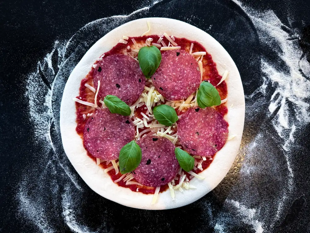 Belegte Pizza mit Trüffelsalami, Käse und Basilikum vor dem Backen