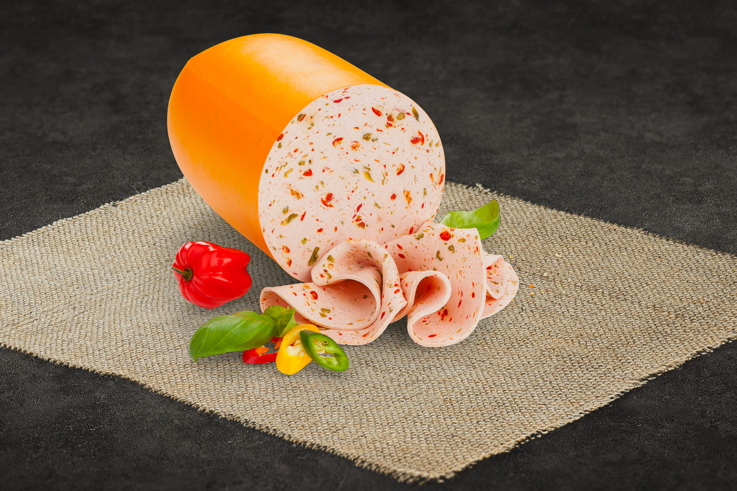 Paprikawurst in Portionsgröße, aufgeschnittene Wurst mit sichtbaren Paprikastückchen auf einem Holzbrett angerichtet, daneben frische Paprika und Kräuter – Produktfoto der Oberpfalz-Beef Paprikawurst für Feinkost und Grillfreunde.