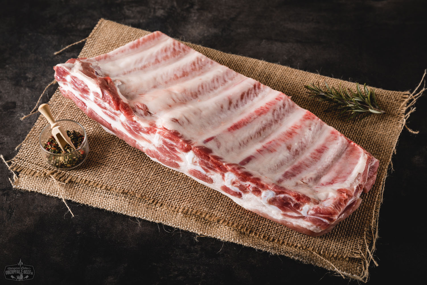 St. Louis Ribs aus der Brustspitze vom Oberpfälzer Landschwein auf Holzbrett – saftiges BBQ-Fleisch regionaler Herkunft St. Louis Ribs vom Oberpfälzer Landschwein, goldbraun gegrillt mit knuspriger Kruste, serviert auf dunklem Holzuntergrund mit frischen Rosmarinzweigen und BBQ-Sauce – hochwertiges Fleischgericht für Grillliebhaber.