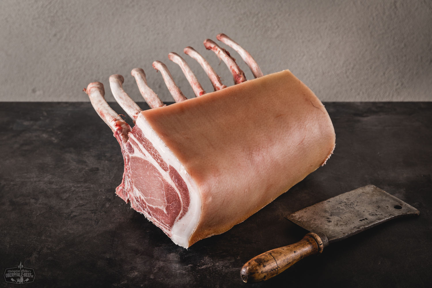 Dry Aged Tomahawk Kotelett vom Oberpfälzer Landschwein – Halbes Stück in Premiumqualität Halbes Dry-Aged Kotelett im Tomahawk-Cut vom Oberpfälzer Landschwein auf dunklem Untergrund, roh mit sichtbarer Marmorierung und langem Rippenknochen – hochwertiges Schweinefleisch für Steak-Zubereitung.