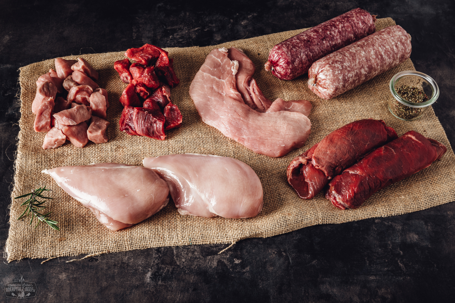 Verschiedene vakuumverpackte Fleischstücke, darunter Rind, Schwein und Wurstwaren, liegen sortiert in einem offenen Pappkarton auf einem Holztisch – die Bauernhof-Box Mixed von Oberpfalz Beef mit regionalem Fleisch in Premiumqualität.