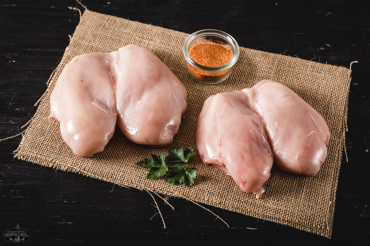 Brustfilet vom Oberpfälzer Bauernhähnchen – Frisches Hähnchenfleisch regionaler Herkunft Rohes Brustfilet vom Oberpfälzer Bauernhähnchen auf dunkler Unterlage, angerichtet mit frischem Rosmarin, Knoblauchzehen, schwarzen Pfefferkörnern und Meersalz – hochwertiges, regionales Hähnchenfleisch für gesundes Kochen.