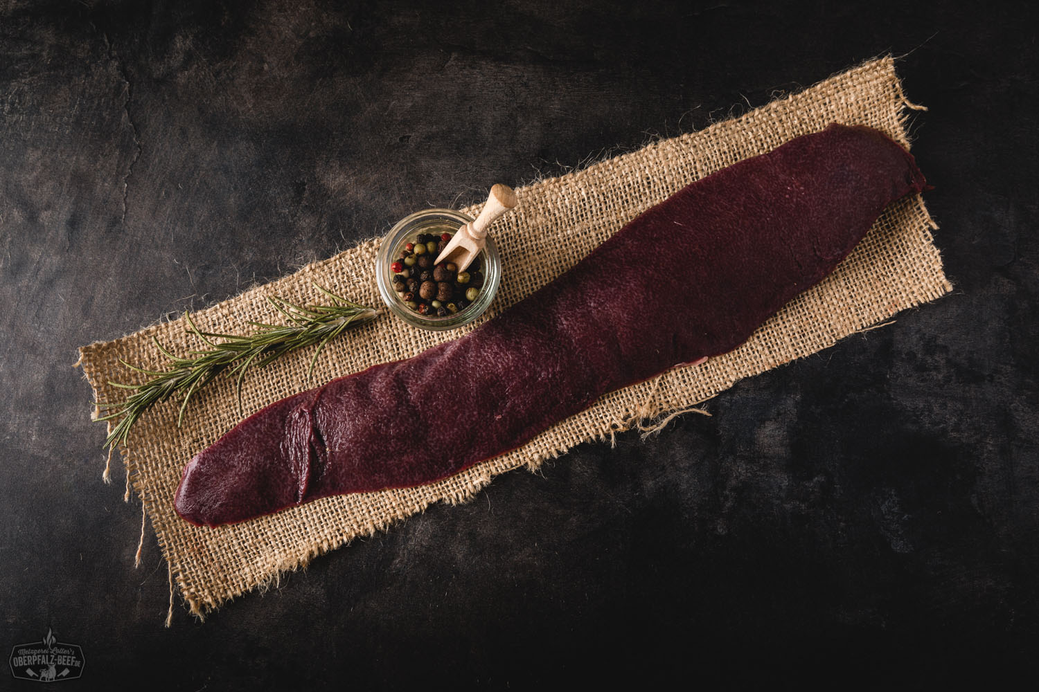 Milz vom Oberpfälzer Landschwein – Frische Schweinemilz aus regionaler Haltung Rohe Milz vom Oberpfälzer Landschwein auf hellem Schneidebrett, umgeben von Rosmarinzweigen, Knoblauch und Pfefferkörnern – hochwertige Innerei in Frischfleischqualität für traditionelle Schweinefleisch-Rezepte.