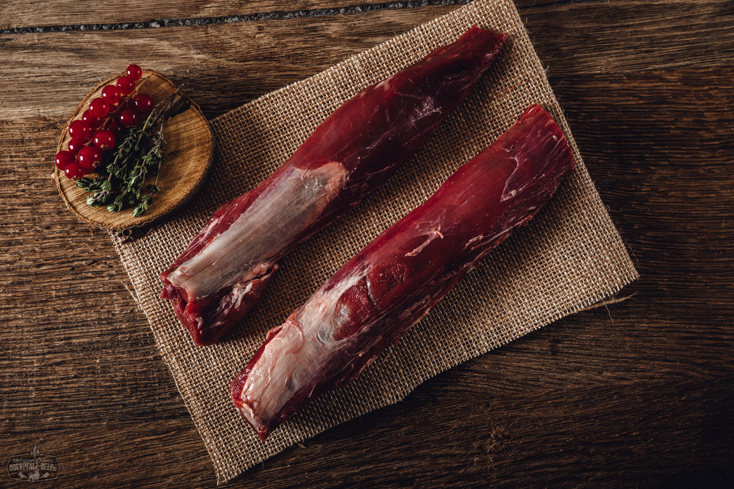 Filet vom Oberpfälzer Wildschwein – Frisches Wildfleisch aus nachhaltiger Jagd Rohes Filetstück vom Oberpfälzer Wildschwein auf dunklem Untergrund, umgeben von Rosmarinzweigen, roten Pfefferkörnern, Meersalz und Knoblauchknolle – stilvoll angerichtet für Fleischliebhaber und Wildfleischkenner.