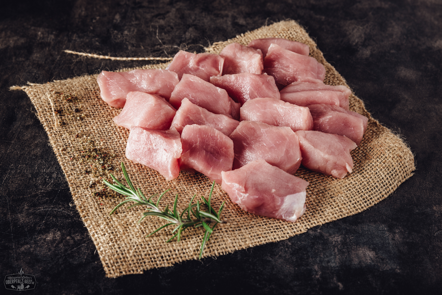Fondue Fleisch aus handgeschnittenem Schweinerücken – zart & hochwertig für geselligen Genuss Handgeschnittenes Fondue-Fleisch vom Schweinerücken, roh und zartrosa, appetitlich angerichtet auf einem dunklen Servierteller mit dekorativen Kräutern und einer kleinen Schale Dip – hochwertiges Fleisch aus der Oberpfalz, ideal für Fondue oder Raclette.
