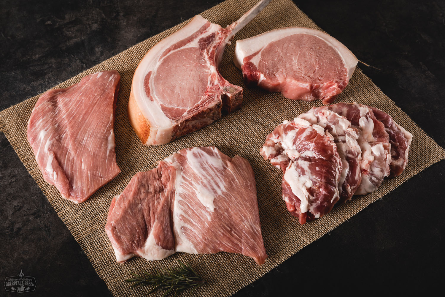 Rohes Schweinefleisch-Steakpaket mit Special Cuts auf dunklem Untergrund angerichtet, darunter verschiedene Zuschnitte wie Nackensteak, Kotelett und Bauchfleisch – hochwertiges Schweinefleisch aus der Oberpfalz, ideal zum Grillen oder Braten.