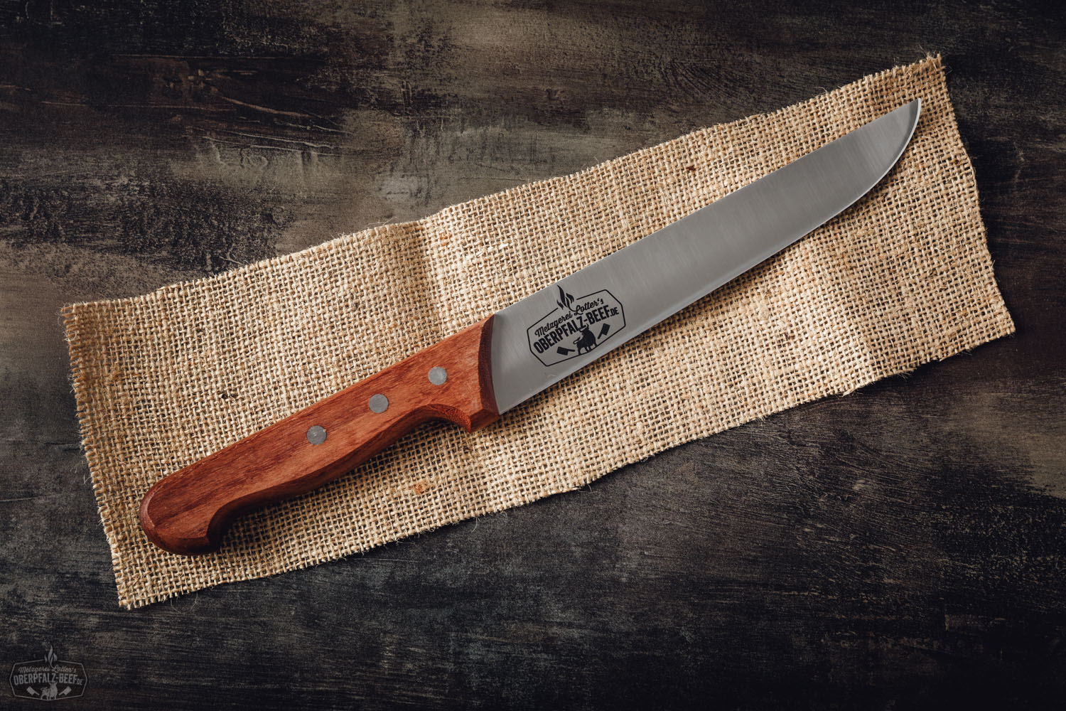 Dick Blockmesser mit Holzgriff im Oberpfalz-Beef-Design, liegend auf dunkler Oberfläche mit sichtbarer Stahlklinge und markantem Logo graviert – ideal für präzises Schneiden von hochwertigem Fleisch.