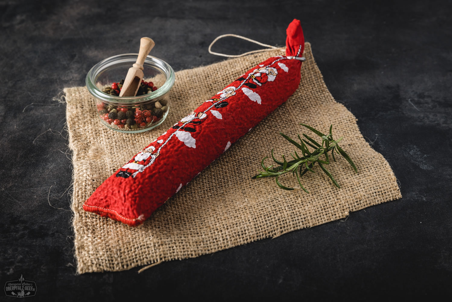 Nikolaus-Salami am roten Band aufgehängt vor hellem Hintergrund, traditionelle Rohwurst in Geschenkform mit rotem Etikett und weihnachtlicher Aufschrift, ideale Delikatesse zu Weihnachten – Oberpfalz-Beef Spezialität.