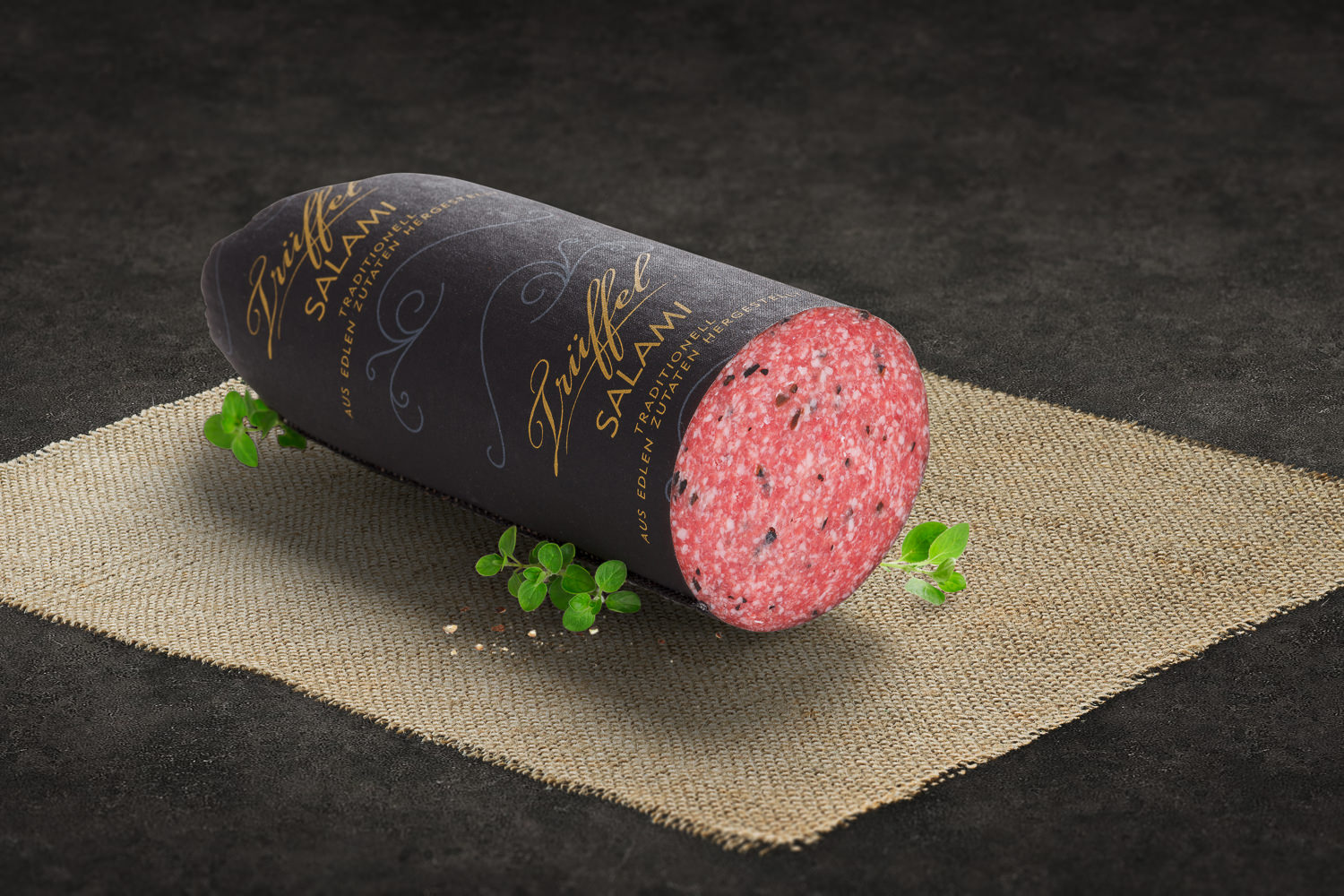 Geschnittene Trüffelsalami auf Holzbrett – Delikatess Wurstspezialität Geschnittene Walnuss-Salami auf Holzbrett angerichtet, mit erkennbaren Walnussstückchen in der Wurst, dekoriert mit frischen Kräutern und stilvoll präsentiert – hochwertige Delikatesse aus regionaler Produktion.