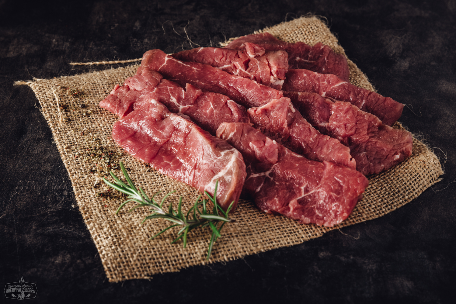 Handgeschnittenes Raclette-Fleisch aus Rinderfilet – hochwertiges Rindfleisch für Raclette und Grill Handgeschnittenes Rinderfilet für Raclette, roh und saftig auf einem dunklen Brett angerichtet, mit feiner Marmorierung und frischen Kräutern garniert – hochwertiges Beef aus der Oberpfalz.