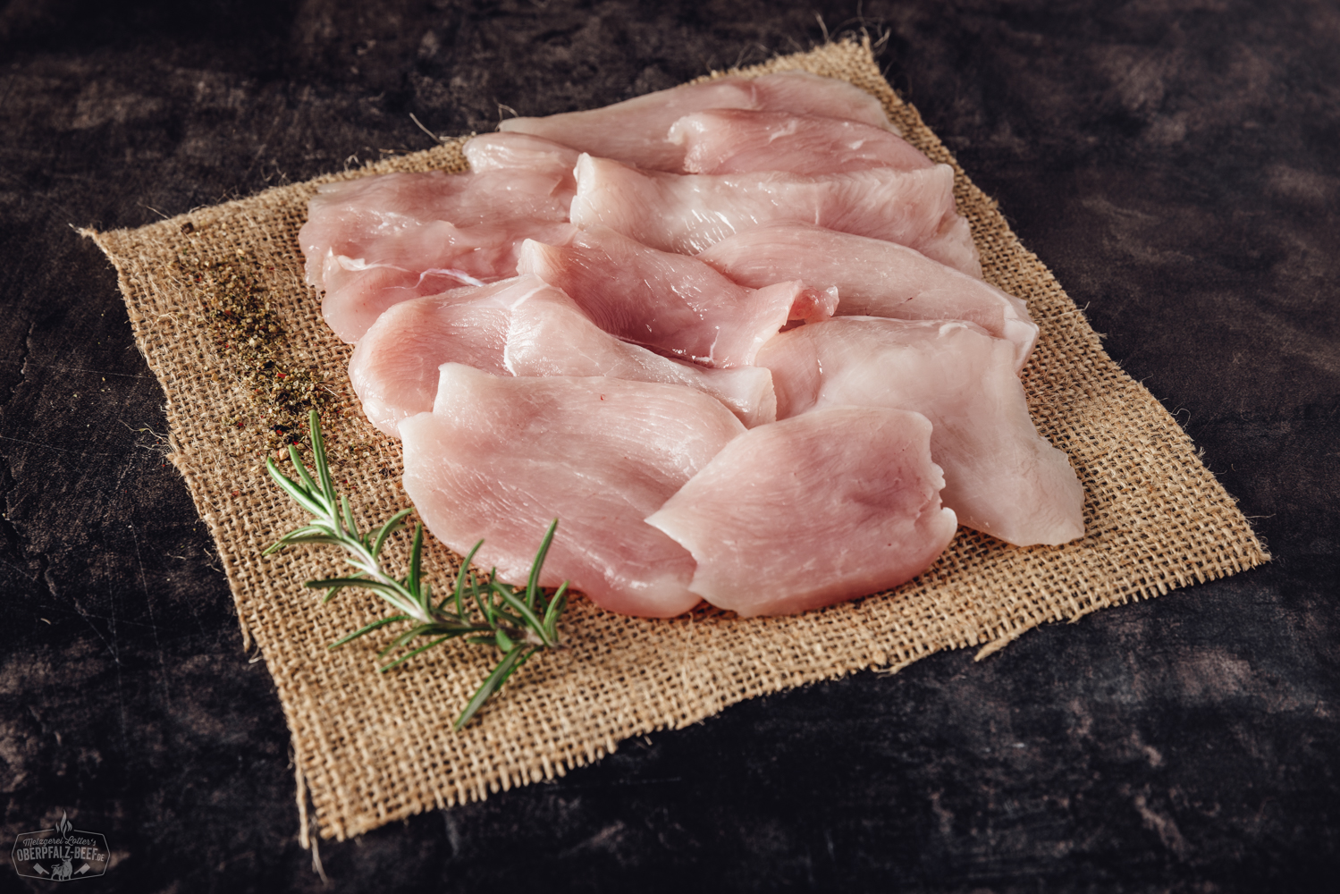 Handgeschnittene Hähnchenbruststreifen auf einem rustikalen Holzbrett, angerichtet für Raclette, mit frischen Kräutern garniert – zartes, hochwertiges Geflügelfleisch ideal für Raclette-Grill oder Pfännchen.