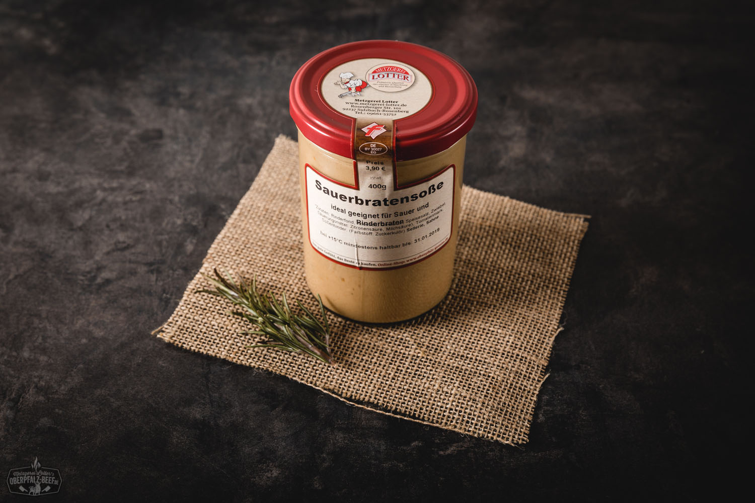 Ein Glas mit dunkler Sauerbratensauce von Oberpfalz Beef steht geöffnet auf einem Holzbrett; daneben frische Kräuter und Gewürze auf rustikalem Untergrund – hochwertige Fertigsauce aus regionaler Herstellung.