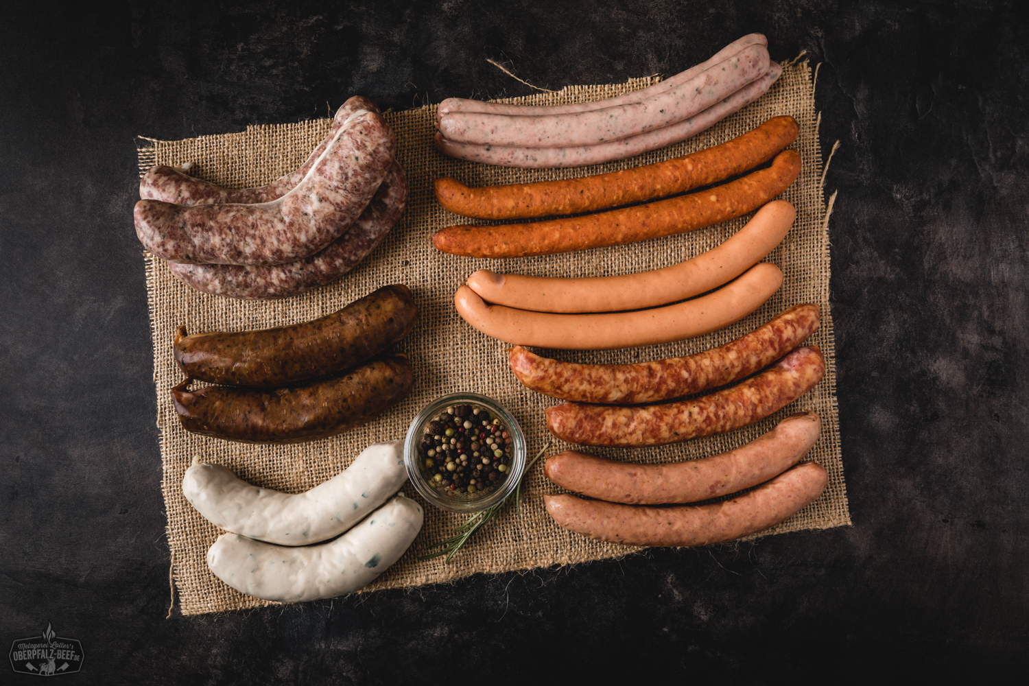 Oberpfälzer Würstchenparade – Auswahl regionaler Bratwürste und Grillwurst vom Metzger Verschiedene Oberpfälzer Wurstspezialitäten, darunter Bratwürste, Wiener und Knacker, dekorativ auf einem rustikalen Holzbrett mit Senf, frischen Kräutern und Brot angerichtet – traditionelles Wurstpaket von Oberpfalz Beef.