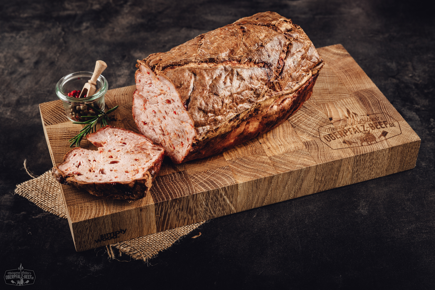 Nahaufnahme eines vakuumverpackten Blocks Pizzakäse zum Selber-Aufbacken von Oberpfalz Beef auf dunklem Hintergrund; deutlich sichtbare, fein geriebene Käsemischung in transparenter Kunststoffverpackung mit gelbem Etikett und schwarzer Schrift.