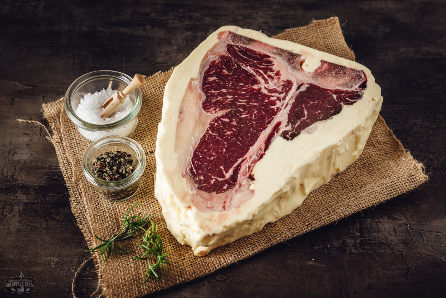 T-Bone-Steak Butter Aged vom Oberpfalz-Rind – Premium Rindfleisch für Grill und Küche T-Bone-Steak vom Oberpfalz-Rind, buttergereift und perfekt gegrillt, mit deutlicher Marmorierung und kräftiger Kruste auf einem dunklen Holzbrett angerichtet – hochwertiges Premiumfleisch in Nahaufnahme, ideal für Grillfans und Steakliebhaber.