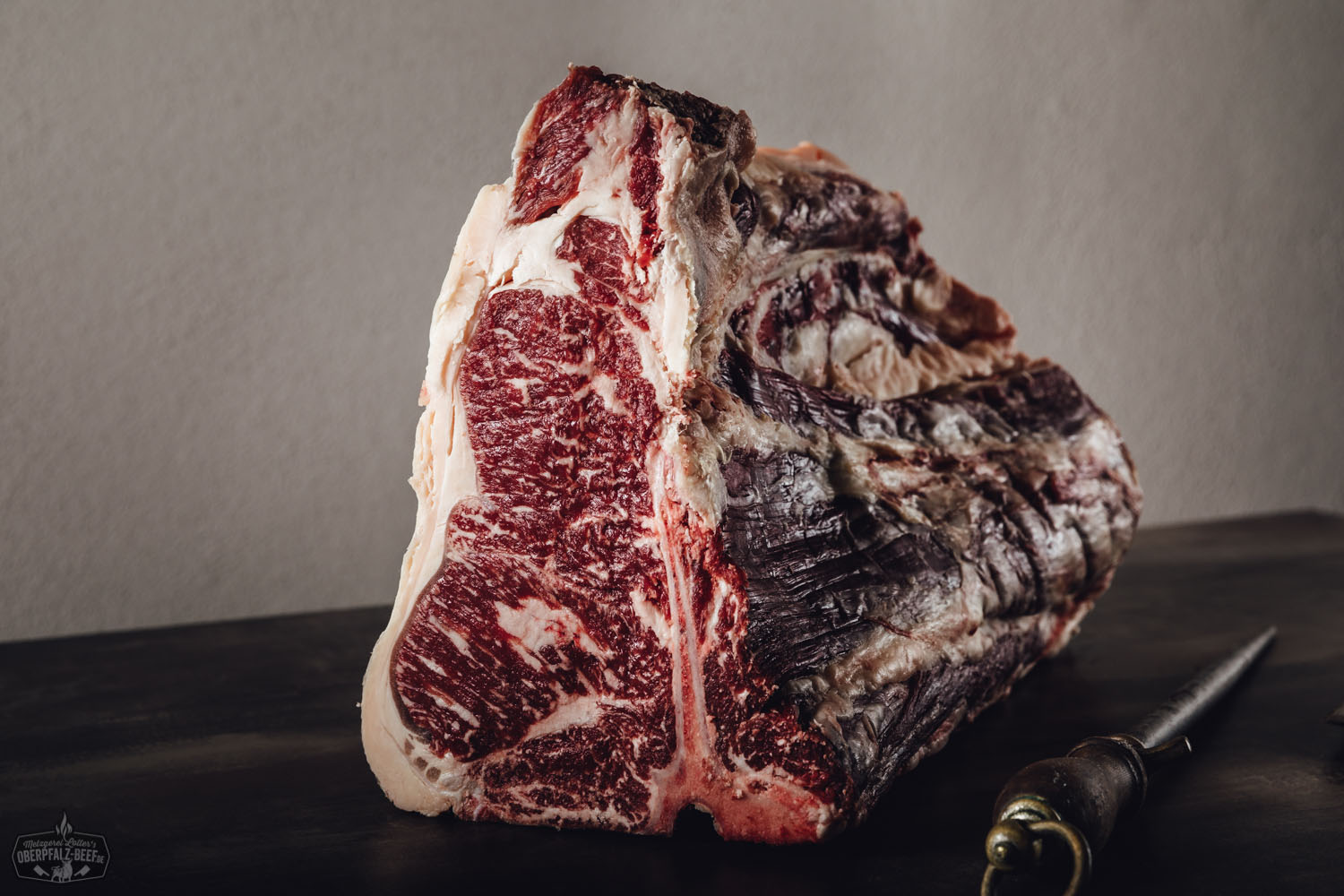 Dry Aged Rindfleisch am Knochen – T-Bone und Porterhouse vom Oberpfalz-Rind Rohes Dry-Aged Rindfleisch am Knochen, speziell ein T-Bone- oder Porterhouse-Cut vom Oberpfalz-Rind, auf schwarzem Untergrund mit Marmorierung und Fettschicht deutlich sichtbar – hochwertiges Fleisch zum Selberreifen.