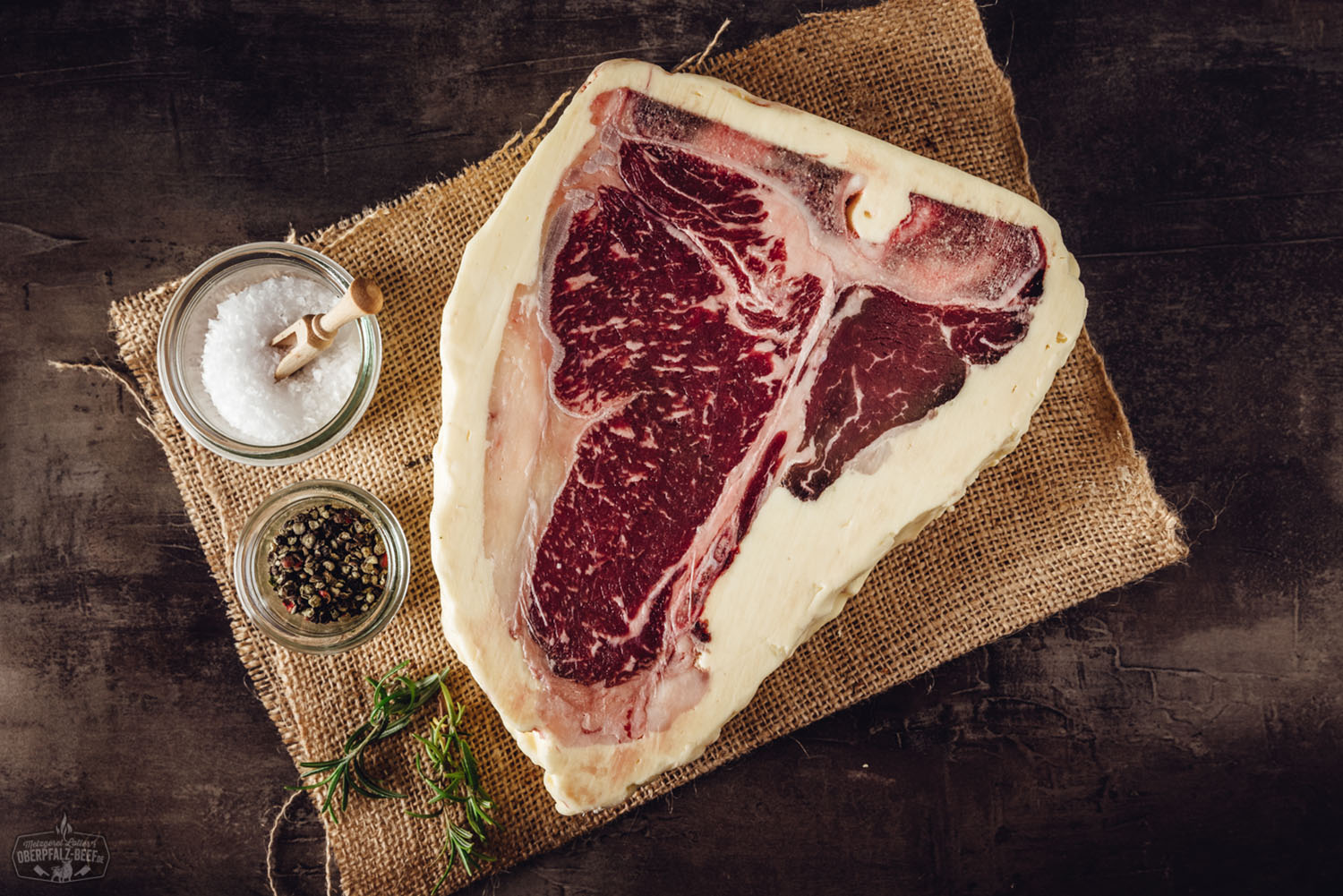 T-Bone-Steak Butter Aged vom Oberpfalz-Rind – Premium Rindfleisch für Grill und Küche T-Bone-Steak vom Oberpfalz-Rind, buttergereift und perfekt gegrillt, mit deutlicher Marmorierung und kräftiger Kruste auf einem dunklen Holzbrett angerichtet – hochwertiges Premiumfleisch in Nahaufnahme, ideal für Grillfans und Steakliebhaber.