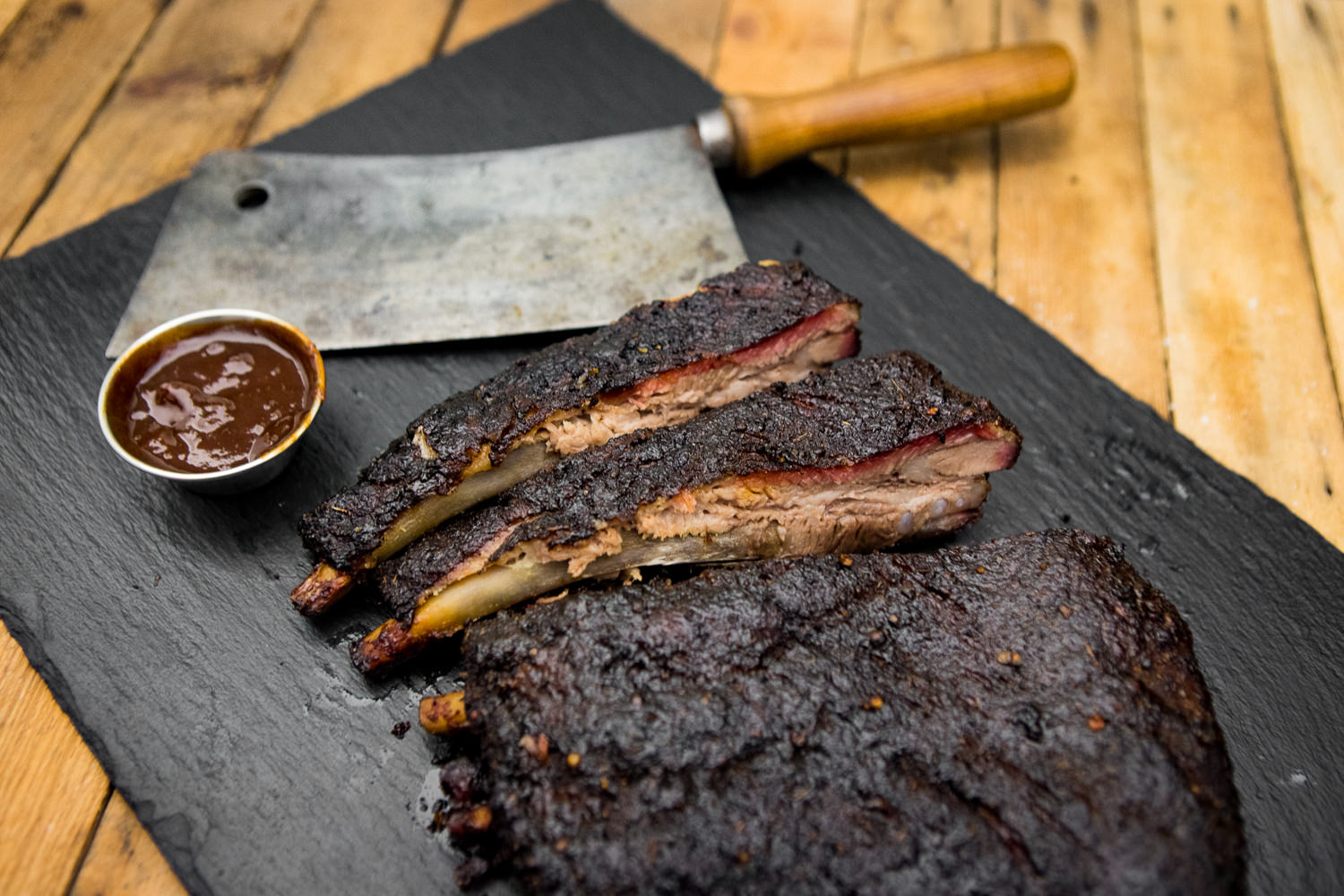 St. Louis Ribs aus der Brustspitze vom Oberpfälzer Landschwein auf Holzbrett – saftiges BBQ-Fleisch regionaler Herkunft St. Louis Ribs vom Oberpfälzer Landschwein, goldbraun gegrillt mit knuspriger Kruste, serviert auf dunklem Holzuntergrund mit frischen Rosmarinzweigen und BBQ-Sauce – hochwertiges Fleischgericht für Grillliebhaber.