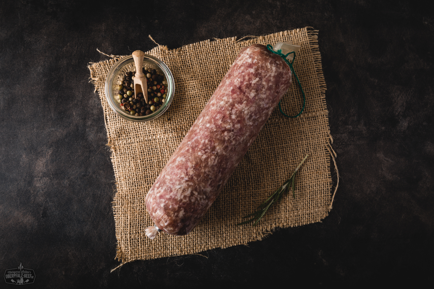 Frisches Schweinehackfleisch roh auf Holzbrett – hochwertiges Hackfleisch aus der Oberpfalz Frisches, grob gewolftes Schweinehackfleisch auf einem dunklen Natursteinbrett, dekoriert mit Rosmarinzweigen, grobem Meersalz, Pfefferkörnern und Knoblauchzehen – hochwertige Zutaten für deftige Fleischgerichte.