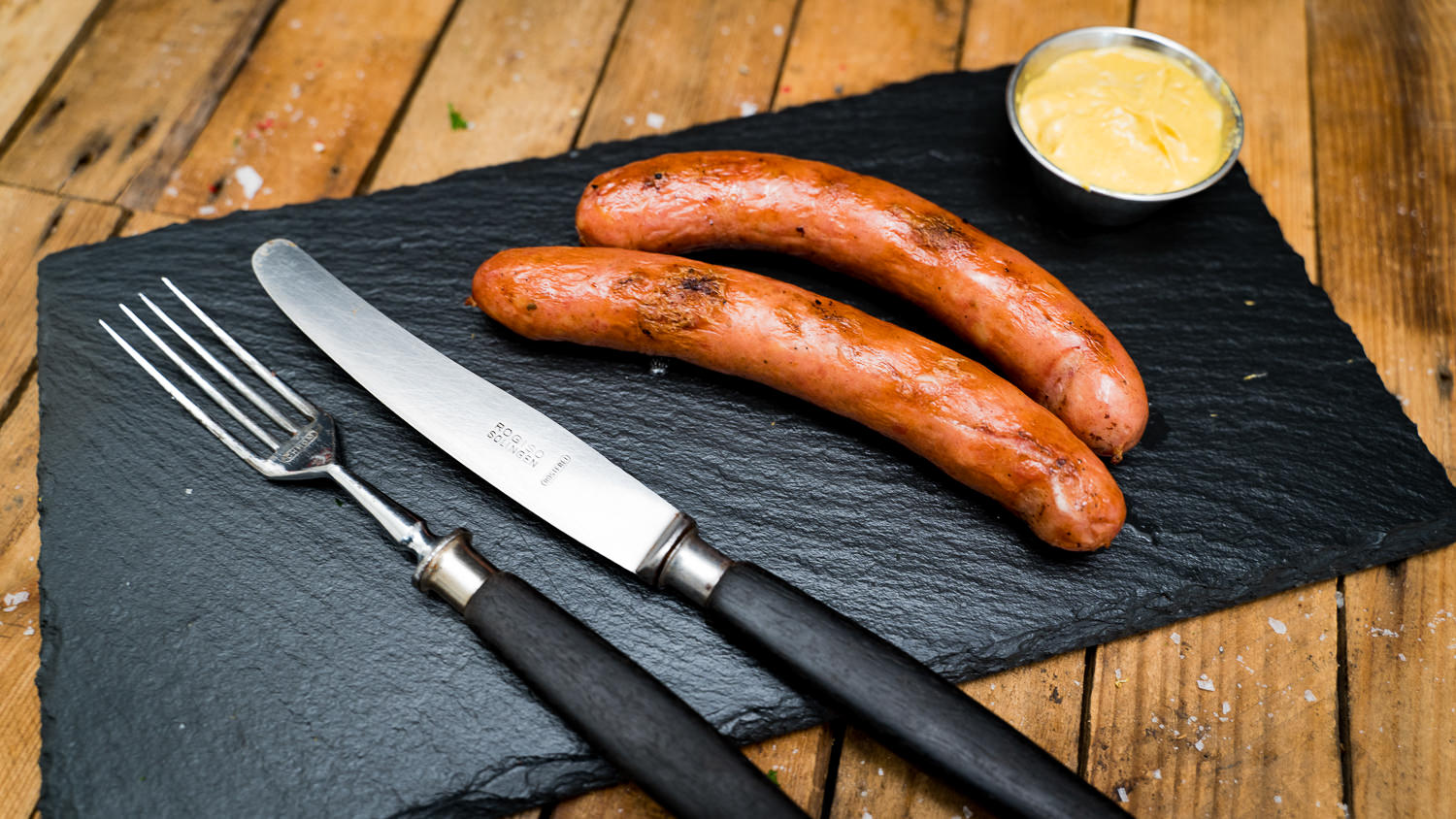Käsegriller vom Grill – Saftige Bratwürste mit geschmolzenem Käsekern Nahaufnahme von fünf gegrillten Käsegrillern mit goldbrauner, knuspriger Haut und sichtbar geschmolzenem Käse in den Anschnitten, serviert auf einem dunklen Holzbrett mit rustikalem Hintergrund – herzhafte Bratwurst-Delikatesse typisch für die Oberpfalz.