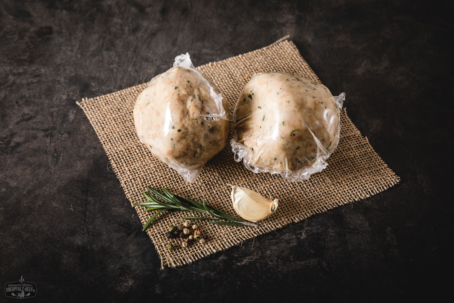 Zwei goldbraun gebratene Semmelknödel auf einem dunklen Teller, angerichtet mit frischer Petersilie und begleitet von einer dunklen Bratensoße, auf rustikalem Holzuntergrund serviert – typisch bayerische Beilage aus altbackenem Brot.