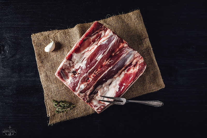 Lammrücken-Kotelett am Stück vom Juradistl-Lamm – regionales Premiumfleisch aus der Oberpfalz Ganzes Lammrücken-Kotelett vom Juradistl-Lamm, roh und mit Knochen, auf Holzbrett angerichtet; saftiges, marmoriertes Fleisch mit rosiger Farbe, natürliche Fettschicht sichtbar, rustikale Darstellung für Fleischliebhaber und Gourmetküche.