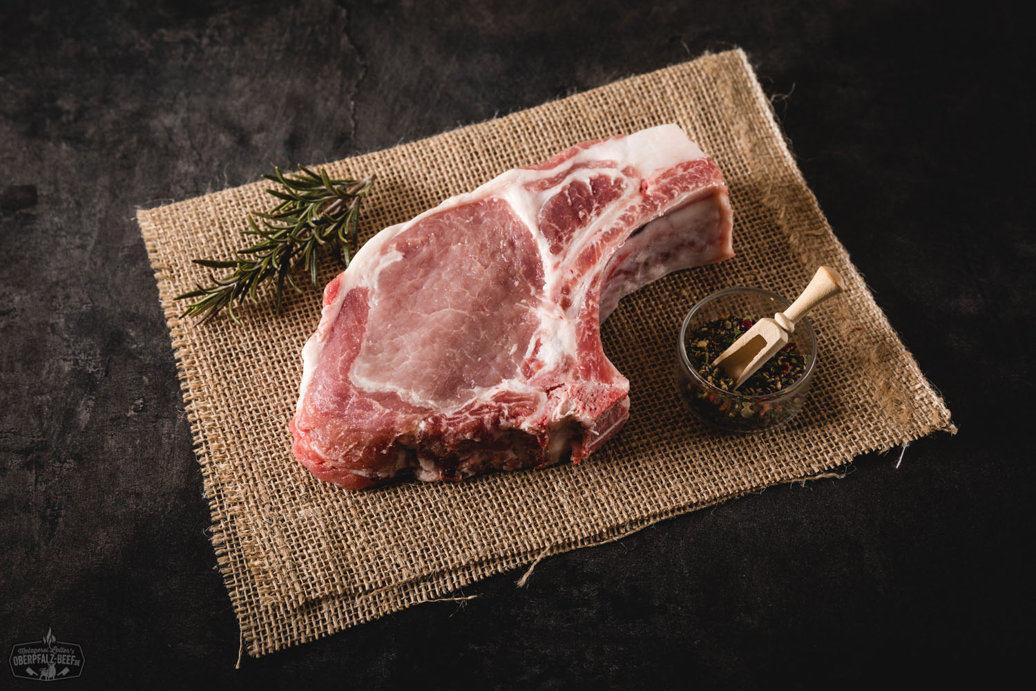 Rohes Metzgerkotelett vom Oberpfälzer Landschwein auf dunklem Untergrund, mit gut sichtbarem Knochen, kräftiger Marmorierung und frischem Fettrand – hochwertiges Schweinefleisch für Grill oder Pfanne.