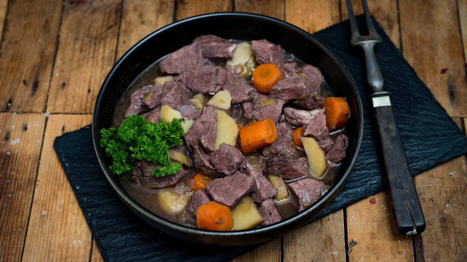 Handgeschnittenes Kalbsgulasch vom Oberpfälzer Milchkalb – Frisches Qualitätsfleisch aus Bayern Handgeschnittenes Gulasch vom Oberpfälzer Milchkalb, roh auf einem dunklen Holzbrett angerichtet, umgeben von Gewürzen wie grobem Salz und Pfeffer, dekoriert mit frischem Rosmarin – hochwertiges Kalbfleisch aus der Region für deftige Fleischgerichte.