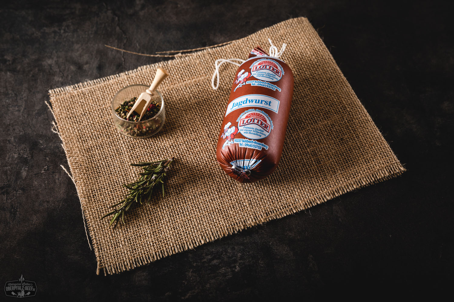 Jagdwurst als Portionswurst in Kunststoffverpackung – Frische Wurstware online kaufen Mehrere vakuumverpackte Portionsstücke Jagdwurst liegen auf einem dunklen Untergrund; jede Wurst ist mit einem weißen Etikett versehen, auf dem "Jagdwurst" und das Logo von Oberpfalz-Beef zu lesen sind.