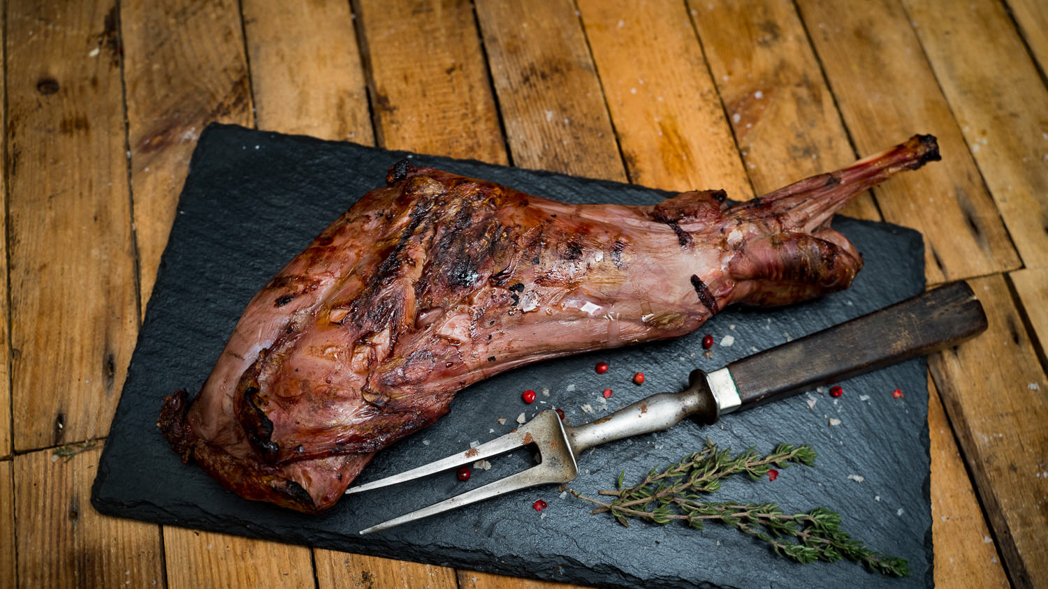 Schulter mit Knochen vom Oberpfälzer Reh – Wildfleisch aus regionaler Jagd Roher Rehschulterbraten mit Knochen vom Oberpfälzer Reh auf dunklem Holzbrett, umgeben von frischen Rosmarinzweigen, Wacholderbeeren und grobem Salz – hochwertiges Wildfleisch für Braten oder Schmorgerichte.