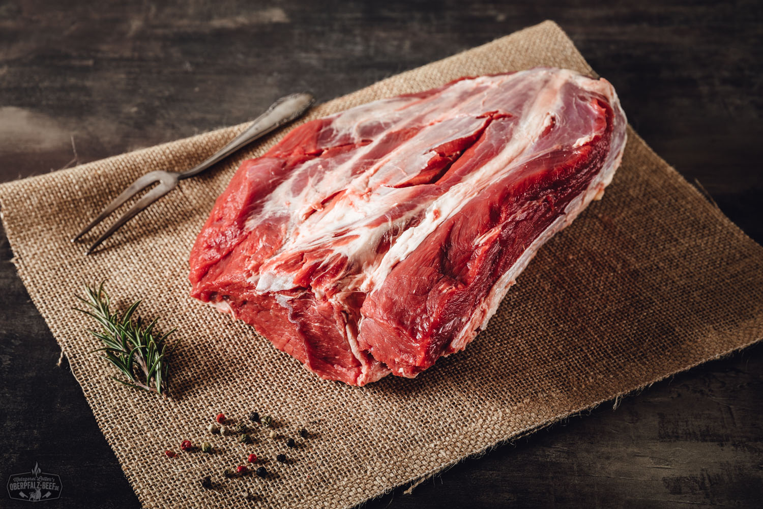 Rohes Suppenfleisch aus der hohen Rippe vom Oberpfalz-Rind, auf einem dunklen Schneidebrett angerichtet, umgeben von frischen Zutaten wie Karotten, Sellerie, Petersilie und Lauch; hochwertige, regionale Fleischware für Rindfleischgerichte und Suppen.