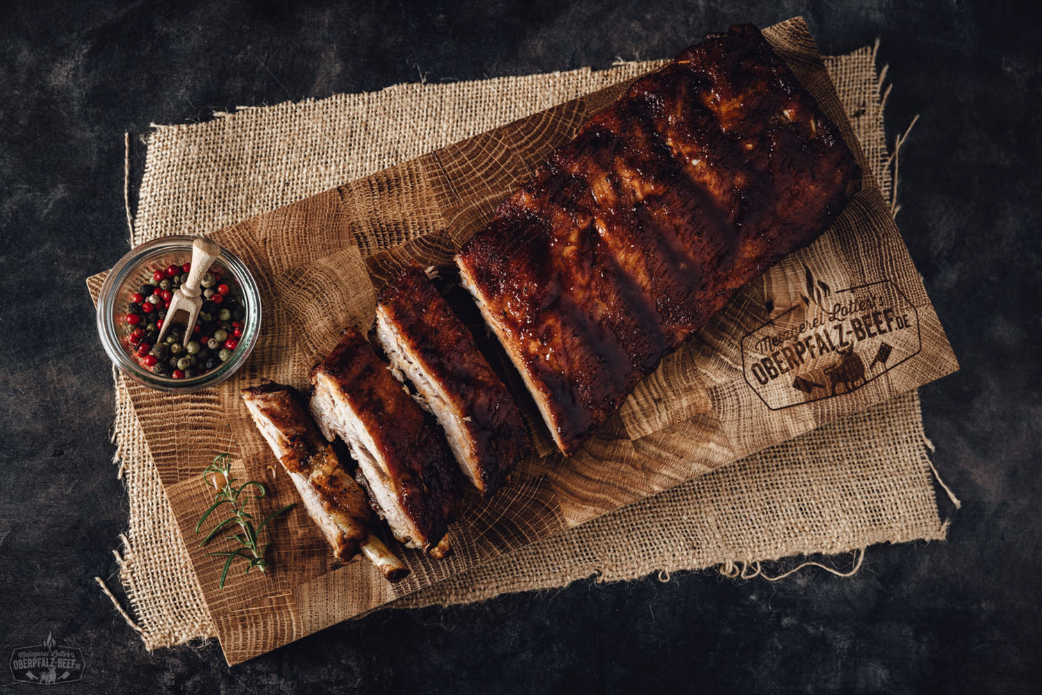 Sous-vide gegarte Baby Back Ribs vom Oberpfälzer Landschwein – zart & BBQ-ready Sous-vide gegarte Baby Back Ribs vom Oberpfälzer Landschwein, knusprig glasiert und serviert auf einem Holzbrett mit frischen Kräutern und Barbecue-Sauce – zartes Fleisch mit rauchiger Note, perfekt zubereitet für BBQ-Liebhaber.