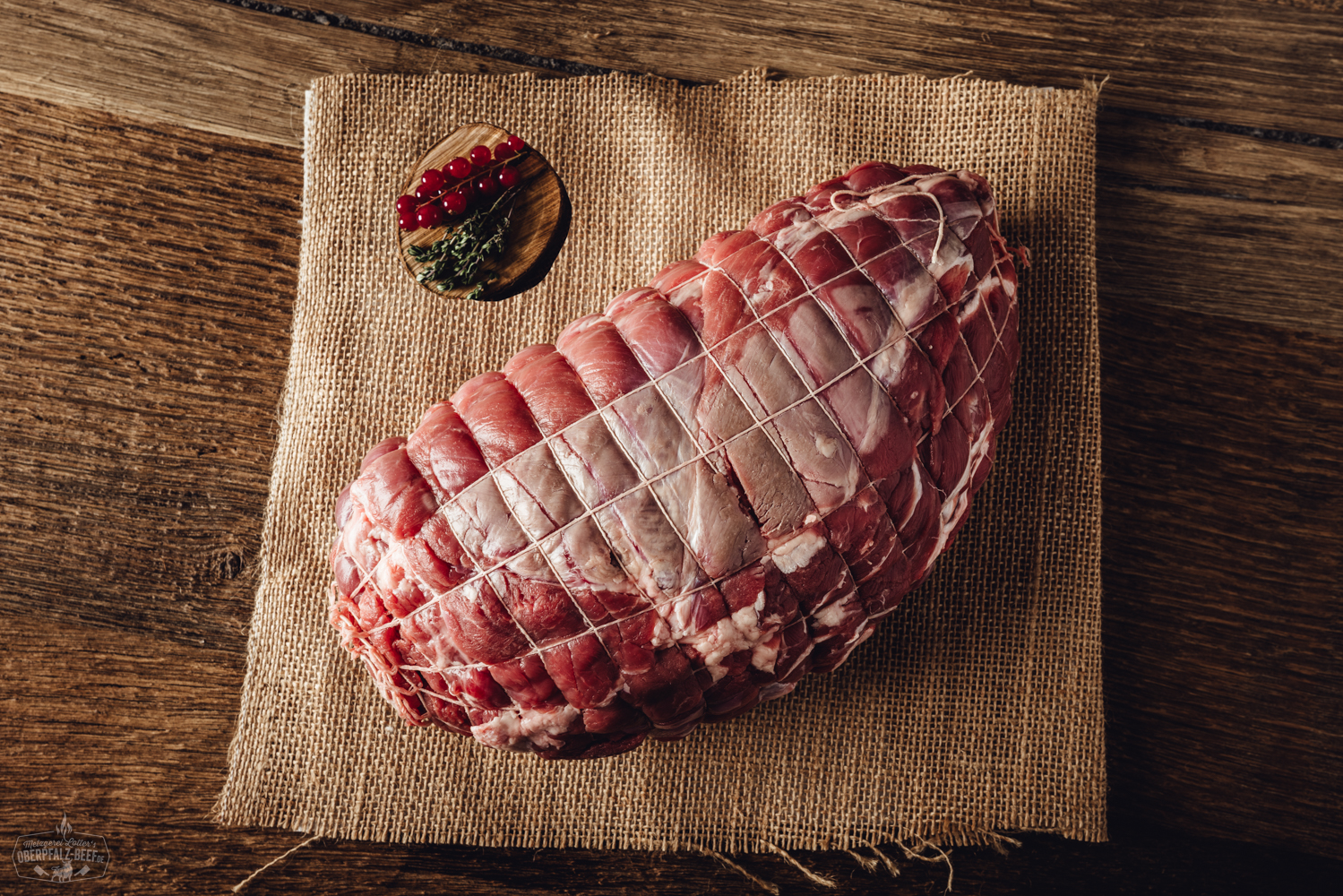 Rollbraten vom Oberpfälzer Wildschwein auf Holzbrett – Wildfleisch Spezialität Rollbraten vom Oberpfälzer Hirsch, angerichtet auf einem Holzbrett mit Rosmarinzweig, Knoblauchzehe und grobem Pfeffer – perfekt gegartes, saftiges Wildfleisch mit gut sichtbarer Füllung, appetitlich aufgeschnitten und rustikal präsentiert.