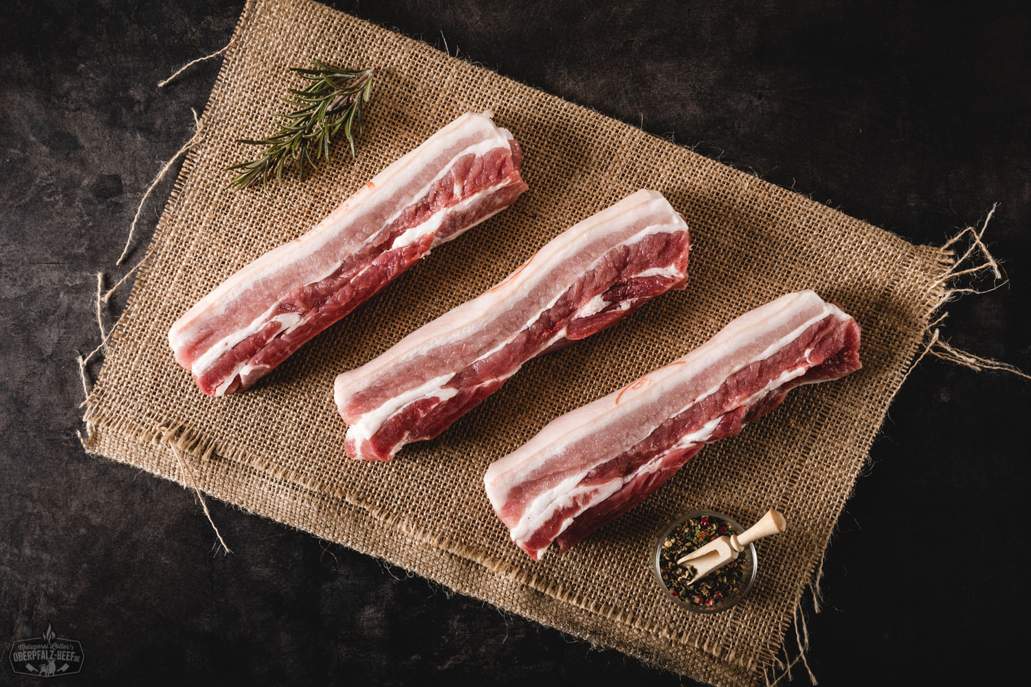 Bauchsteaks vom Oberpfälzer Landschwein – naturbelassen und frisch Rohes Bauchsteak vom Oberpfälzer Landschwein auf schwarzer Steinplatte angerichtet, mit frischen Kräutern, Knoblauchzehen und Pfefferkörnern garniert – hochwertiges regionales Schweinefleisch für Grill oder Pfanne.