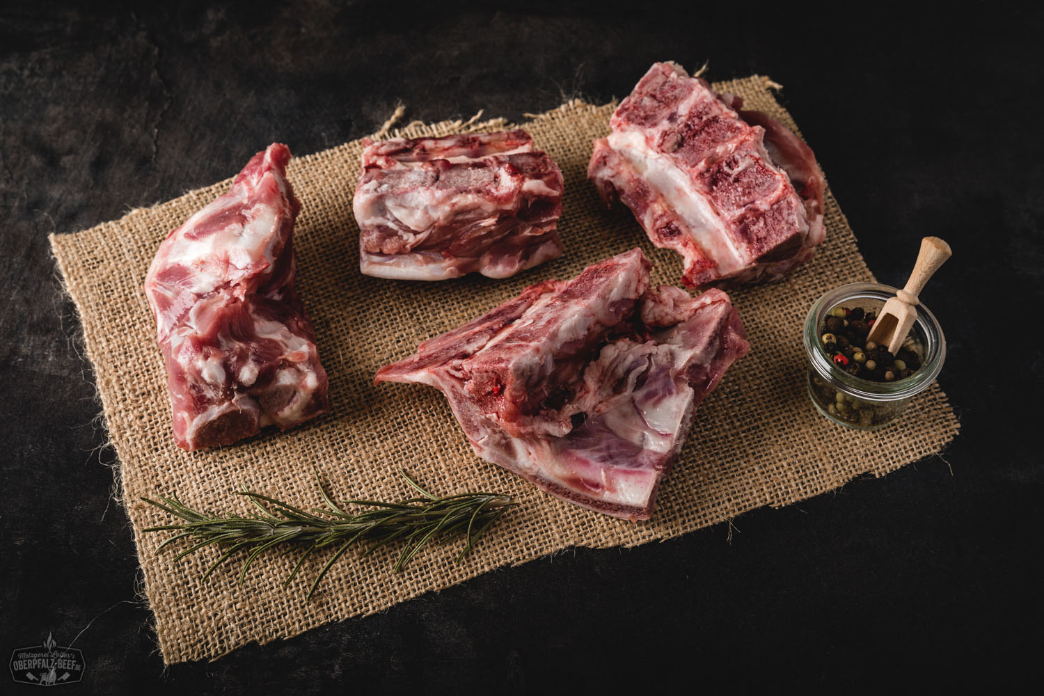 Rohes Schweinefleisch vom Oberpfälzer Landschwein, in frischen, saftigen Stücken auf einem dunklen Untergrund präsentiert, umgeben von Gewürzen wie Rosmarin, Knoblauch und Pfefferkörnern – hochwertiges regionales Fleisch für bewussten Fleischgenuss.