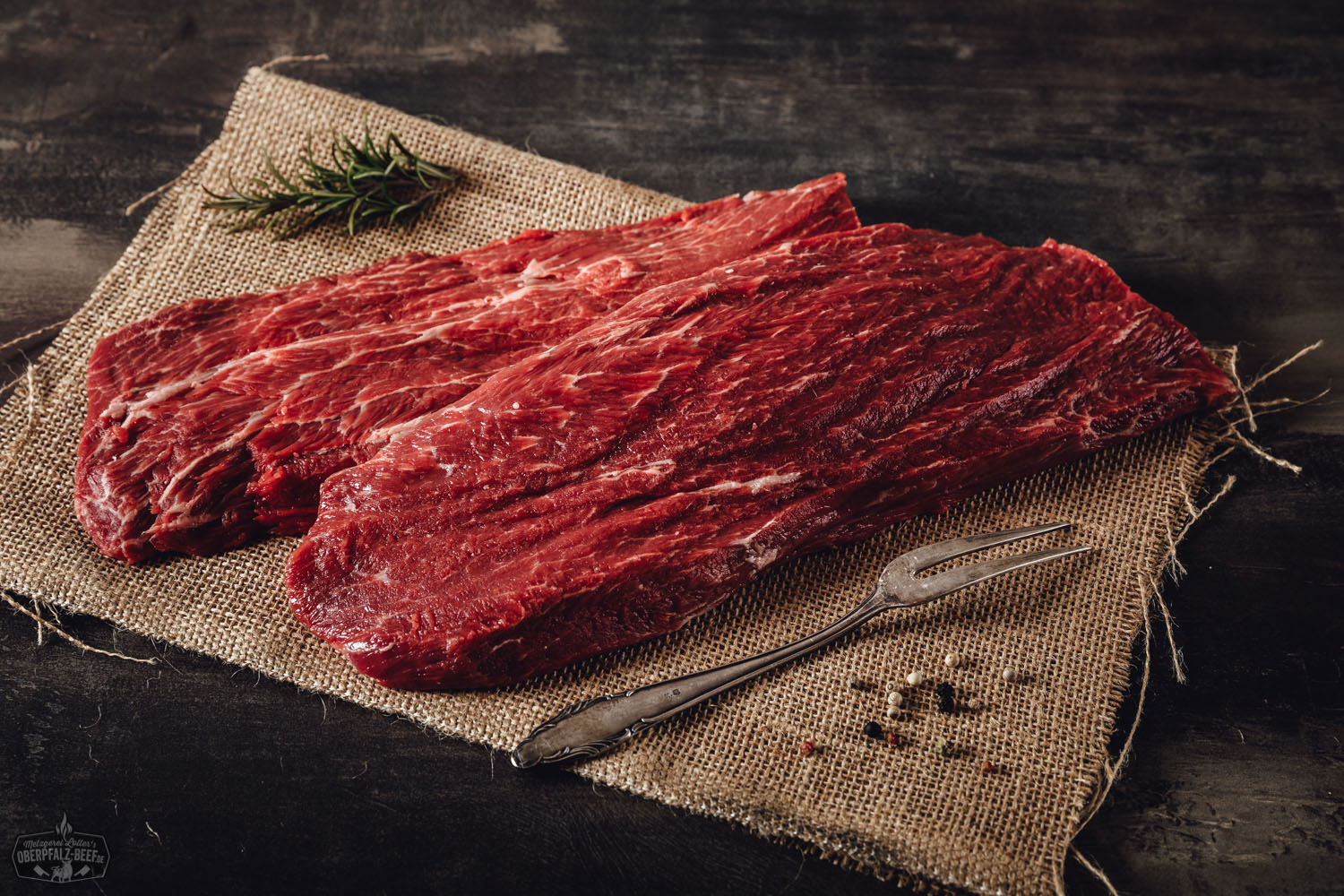 Rohes Flat Iron Steak vom Oberpfalz-Rind auf dunklem Untergrund, hell ausgeleuchtet; das fein marmorierte, gleichmäßig geschnittene Stück Fleisch liegt bereit zum Zubereiten – perfekte Fleischstruktur und Frische für hochwertiges Rindfleisch-Erlebnis.