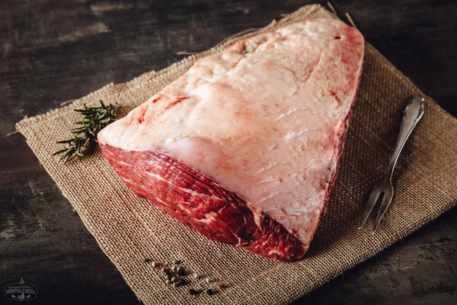 Rohes Picanha-Steak vom Oberpfalz-Rind liegt auf einem dunklen Holzbrett, umgeben von grobem Meersalz, frischen Kräutern und Knoblauch; hochwertiges Wet Aged Beef mit deutlicher Marmorierung – ideale Fleischqualität für Steakliebhaber.