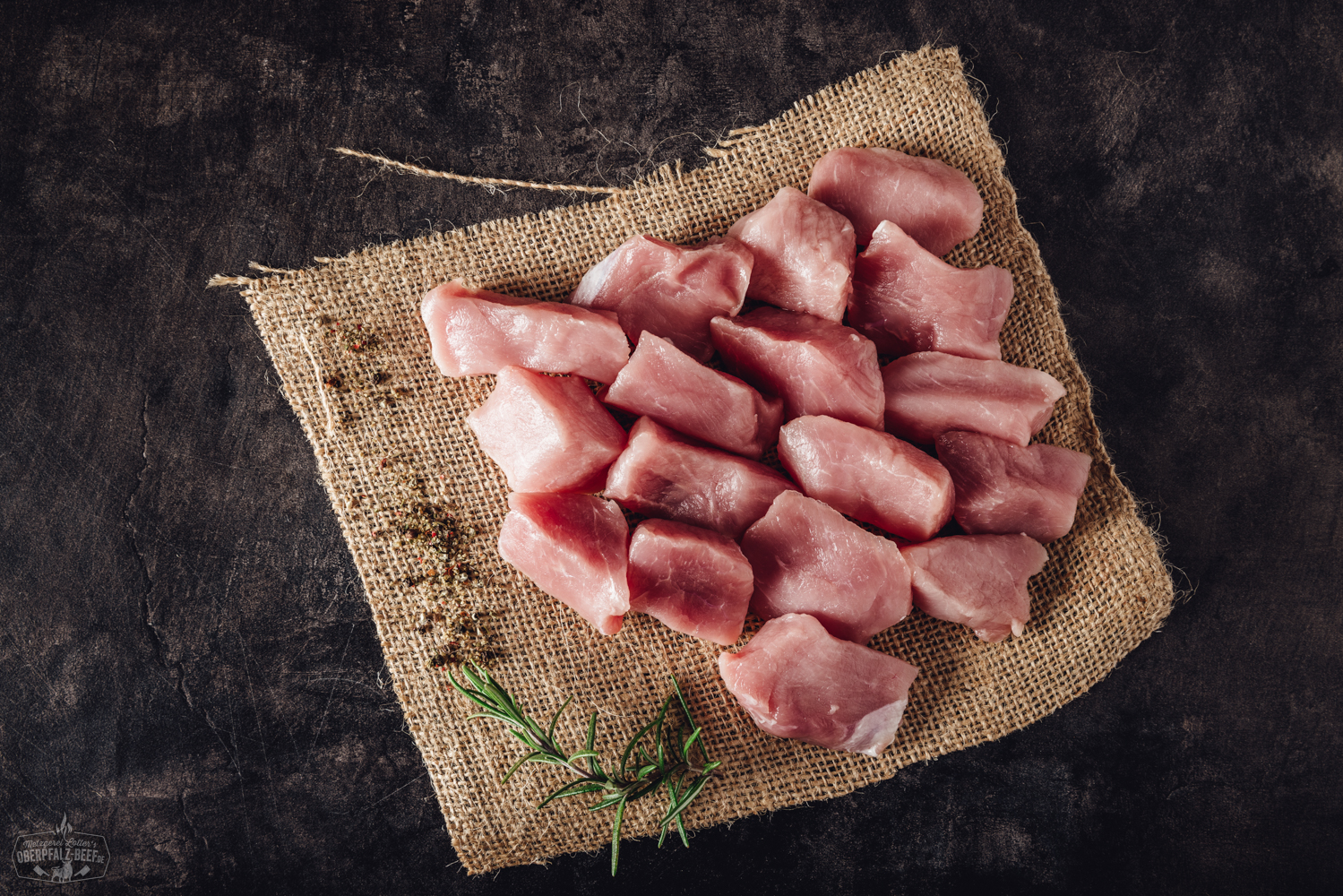 Fondue Fleisch aus handgeschnittenem Schweinerücken – zart & hochwertig für geselligen Genuss Handgeschnittenes Fondue-Fleisch vom Schweinerücken, roh und zartrosa, appetitlich angerichtet auf einem dunklen Servierteller mit dekorativen Kräutern und einer kleinen Schale Dip – hochwertiges Fleisch aus der Oberpfalz, ideal für Fondue oder Raclette.