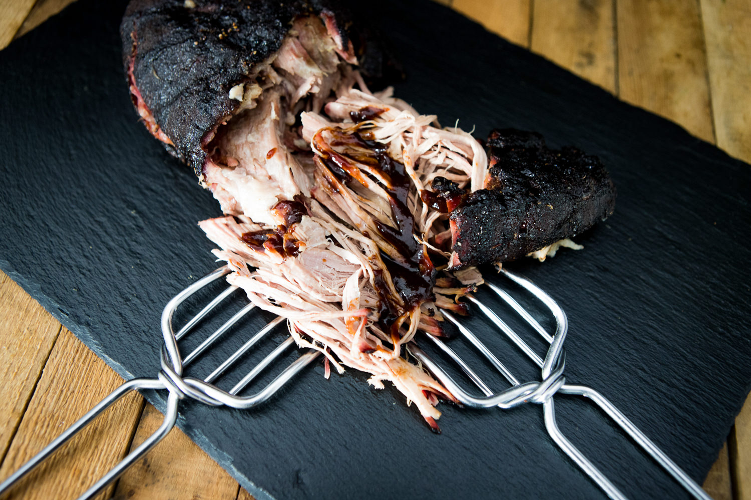 Pulled Pork Schulter mit Knochen vom Oberpfälzer Landschwein – Regionales Qualitätsfleisch Rohe Schweineschulter mit Knochen vom Oberpfälzer Landschwein, auf einer schwarzen Schieferplatte angerichtet; das gut marmorierte Fleisch mit sichtbaren Fettstrukturen liegt neben Kräutern, Gewürzen und einem Messer – ideal für Pulled Pork Zubereitung.