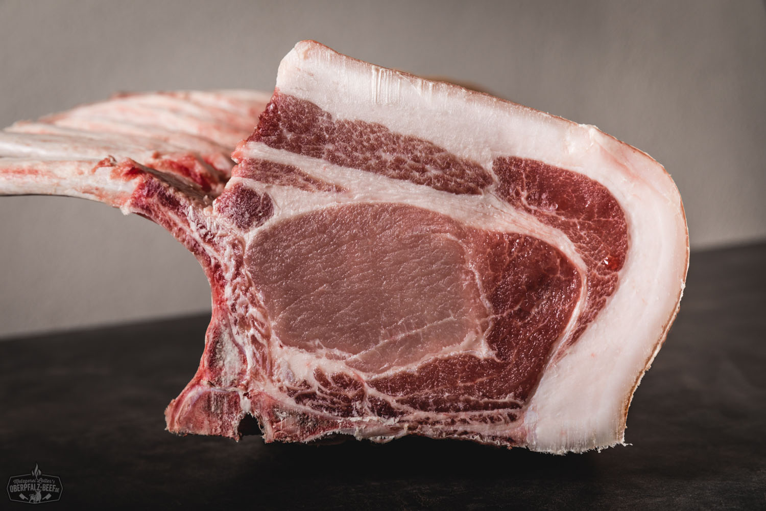 Tomahawk-Kotelett vom Oberpfälzer Landschwein – Frisch & Regional Frisches Tomahawk-Kotelett vom Oberpfälzer Landschwein roh auf dunklem Holzuntergrund, mit deutlich sichtbarem langen Rippenknochen, marmorierter Fleischstruktur und kräftiger roter Farbe; ideales Premiumstück für Grill oder Pfanne.