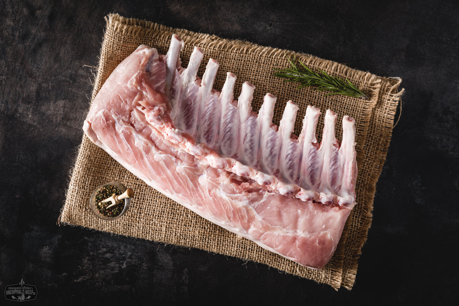 Spanferkelracks vom Oberpfälzer Landschwein, knusprig gebraten mit goldbrauner Kruste, serviert auf rustikalem Holzbrett und garniert mit frischen Kräutern – perfektes Grillgericht aus regionaler Zucht.