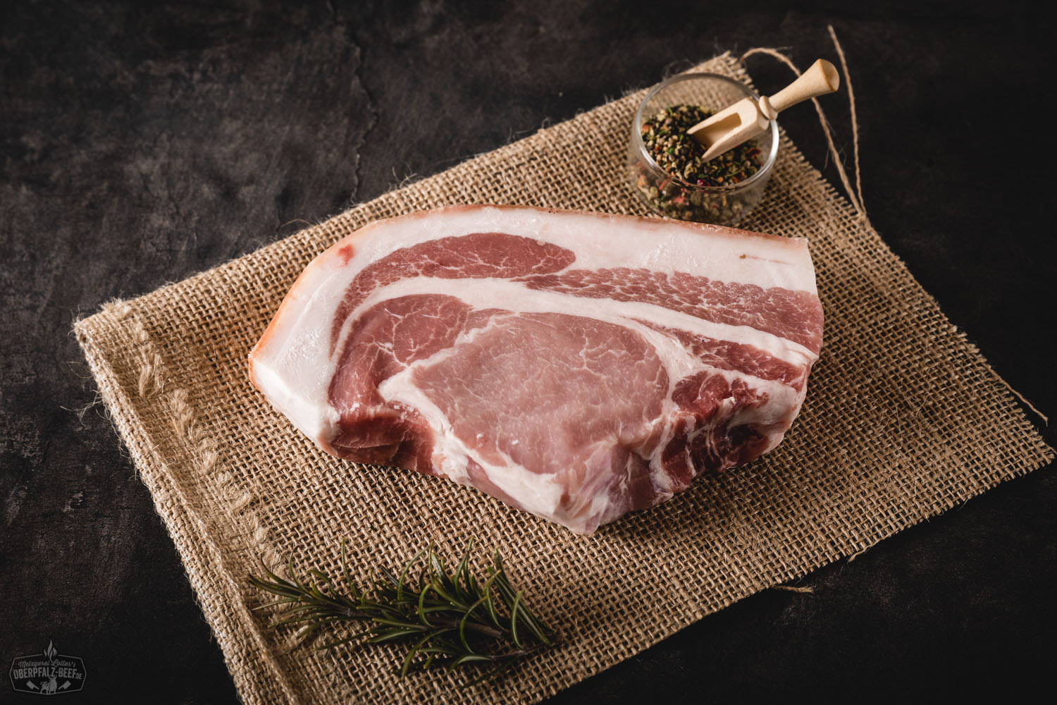 Entrecôte-Steak vom Oberpfälzer Landschwein – zart, saftig und regional Rohes Entrecôte-Steak vom Oberpfälzer Landschwein auf dunklem Untergrund, marmoriert mit feinen Fettadern, daneben frische Rosmarinzweige, grobes Meersalz und rote Pfefferkörner – hochwertige Fleischqualität für BBQ oder Braten.