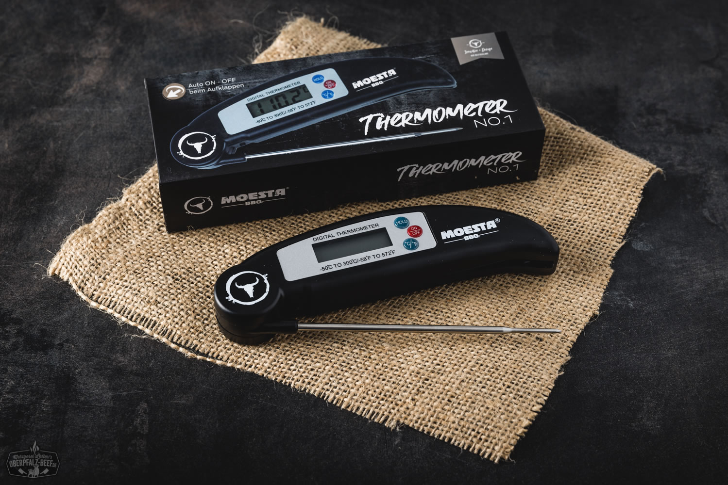 Moesta Grill- und Bratenthermometer No. 1 mit digitaler Anzeige, schwarzem Gehäuse und farbigem Display, auf einem dunklen Hintergrund professionell in Szene gesetzt – ideales BBQ-Zubehör zur präzisen Fleischtemperaturmessung.