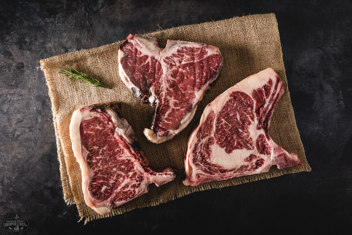 Dry Aged Bone-in Steak vom Oberpfalz-Rind – Premium Fleischqualität Trocken gereifte Bone-in-Steaks vom Oberpfalz-Rind roh auf schwarzem Untergrund angerichtet, mit sichtbarer Marmorierung und Knochen, hochwertiges Dry Aged Beef für Grill und Feinschmecker.