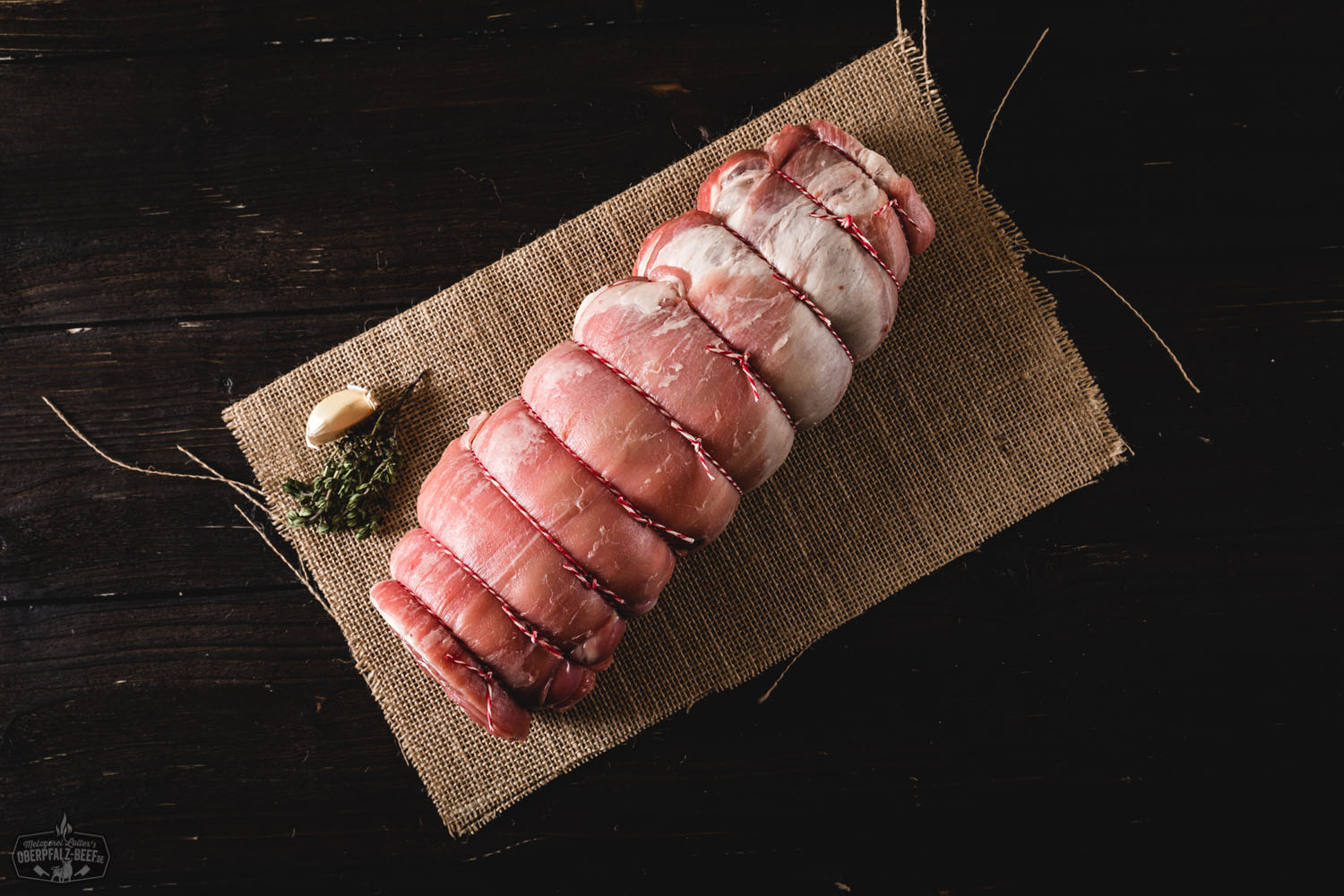 Saftig gebratener Lammrollbraten aus der Schulter vom Juradistl-Lamm, frisch aufgeschnitten auf einem Holzbrett angerichtet, umgeben von Kräutern und Gewürzen – hochwertiges Bio-Fleisch aus der Oberpfalz.