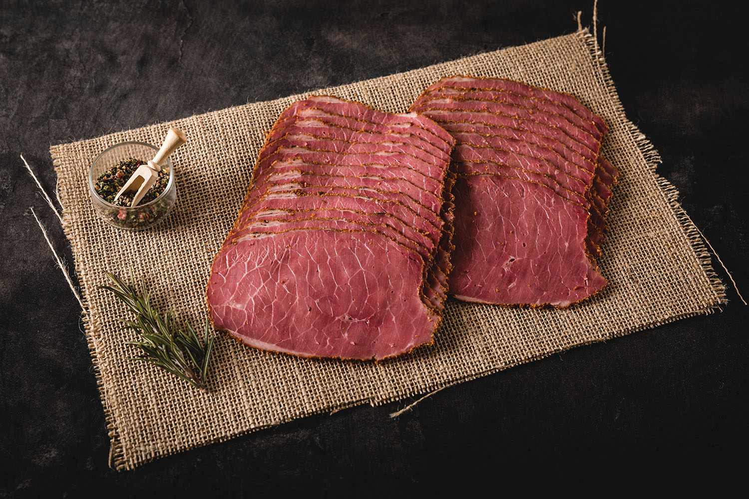 Geschnittenes Pastrami im Oberpfalz-Style, saftig und zartrosa, auf einem Holzbrett angerichtet mit sichtbarem Gewürzrand und zarter Marmorierung – traditionelles bayerisches Rindfleisch-Delikatessprodukt für Feinschmecker.